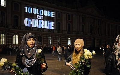 Women give out white roses near the Capitole building in Toulouse, southern France, where on the facade is projected the words "Toulouse est Charlie" (Toulouse is Charlie), on January 9, 2015 (Photo credit: Remy Gabalda/AFP)