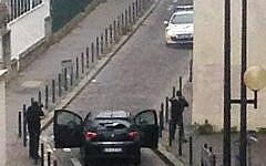 Armed gunmen face police officers near the offices of the French satirical newspaper Charlie Hebdo in Paris on January 7, 2015, during an attack on the offices of the newspaper which left 12 dead, including two police officers. (Photo credit: AFP/ ANNE GELBARD)