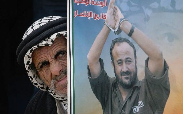 A Palestinian man stands behind a poster depicting jailed Fatah leader Marwan Barghouti, Ramallah, February 28, 2012. (Issam Rimawi/Flash90)