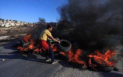 Illustration. A Palestinian youth from the Jalazoun refugee camp places burning tires on the road leading to the settlement of Bet El near Ramallah as he clashes with Israeli soldiers, October 24, 2014 (STR/Flash90) Illustration. A Palestinian youth from the Jalazoun refugee camp places burning tires on the road leading to the settlement of Bet El near Ramallah as he clashes with Israeli soldiers, October 24, 2014 (STR/Flash90)
