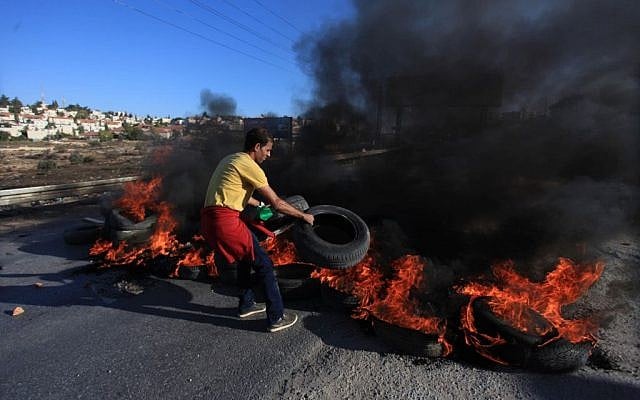 Illustration. A Palestinian youth from the Jilazoun refugee camp places burning tires on the road leading to the settlement of Bet El near Ramallah as he clashes with Israeli soldiers, October 24, 2014 (STR/Flash90) Illustration. A Palestinian youth from the Jilazoun refugee camp places burning tires on the road leading to the settlement of Bet El near Ramallah as he clashes with Israeli soldiers, October 24, 2014 (STR/Flash90)