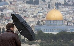 A tourist takes cover under umbrella while visiting the Mount of Olives overlooking Jerusalem's Old City and the Dome of the Rock, on a stormy day, January 3, 2015. (photo credit: Yonatan Sindel/Flash90)