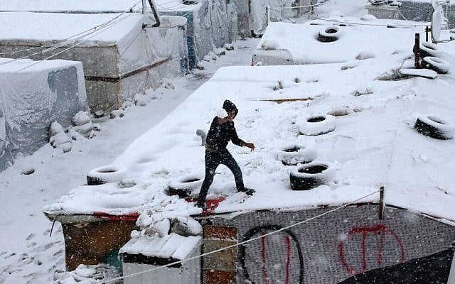 A Syrian boy throws snow from the top of his tent at a refugee camp in Deir Zannoun village, in the Bekaa valley, east Lebanon, Wednesday, Jan. 7, 2015. (Photo credit: AP/Hussein Malla)