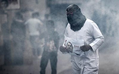 A Bahraini protestor takes cover from tear gas during clashes with riot police following a protest against the arrest of the head of the banned Shiite opposition movement Al-Wefaq, Sheikh Ali Salman (on the poster) on January 1, 2015, in Bilad al-Qadeem, a suburb of Manama. (AFP PHOTO / MOHAMMED AL-SHAIKH)