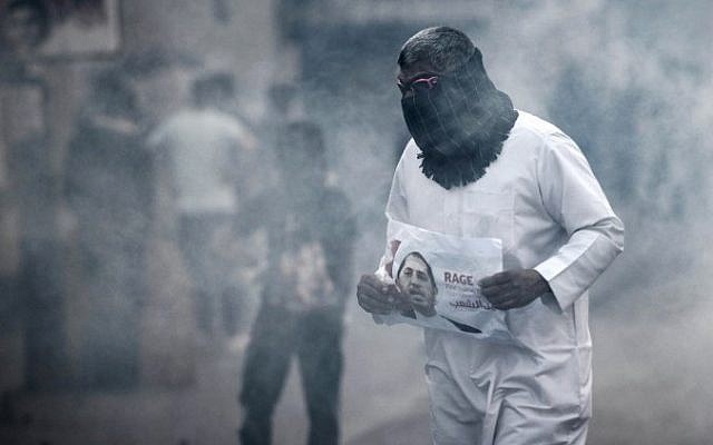 A Bahraini protestor takes cover from tear gas during clashes with riot police following a protest against the arrest of the head of the banned Shiite opposition movement Al-Wefaq, Sheikh Ali Salman (on the poster) on January 1, 2015, in Bilad al-Qadeem, a suburb of Manama. (AFP PHOTO / MOHAMMED AL-SHAIKH) A Bahraini protestor takes cover from tear gas during clashes with riot police following a protest against the arrest of the head of the banned Shiite opposition movement Al-Wefaq, Sheikh Ali Salman (on the poster) on January 1, 2015, in Bilad al-Qadeem, a suburb of Manama. (AFP PHOTO / MOHAMMED AL-SHAIKH)