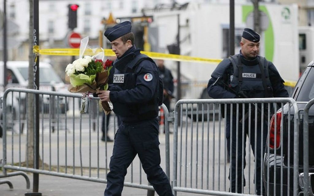 A policeman carries flowers brought by people in front of a kosher grocery store in Porte de Vincennes, eastern Paris, on January 10, 2015 (photo credit: AFP / KENZO TRIBOUILLARD)