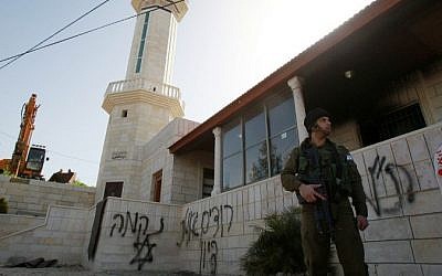 An Israeli soldier stands guard outside a mosque that was torched overnight with anti-Arab slogans in Hebrew sprayed on its walls, in the West Bank village of al-Jaba, southwest of Bethlehem, February 25, 2015. (photo credit: AFP/MUSA AL-SHAER) 