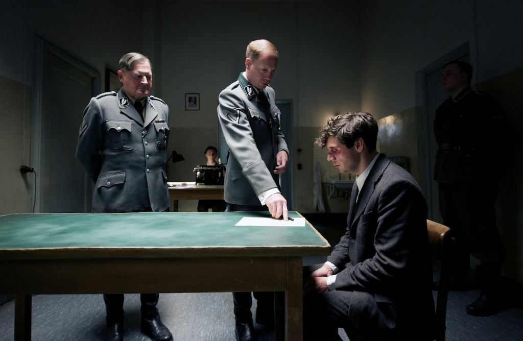 In a scene from 'Elser: 13 Minutes,' Nazi police chief Arthur Nebe (played by Burghart Klaussner), left, and Gestapo head Heinrich Muller (Johann von Bulow) interrogate a beaten Georg Elser (Christian Friedel). (Lucky Bird Pictures/Bernd Schuller)