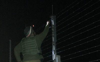 A Kometz soldier, standing on a ladder on the Gaza side of the barrier, fixing the fence (photo credit: Netta Asner/IDF Spokesperson's Unit)