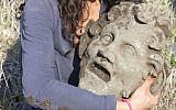 A member of the archaeological team holds the bronze mask of the god Pan, uncovered at the University of Haifa’s excavation at Hippos-Sussita. (photo credit: JTA via University of Haifa)