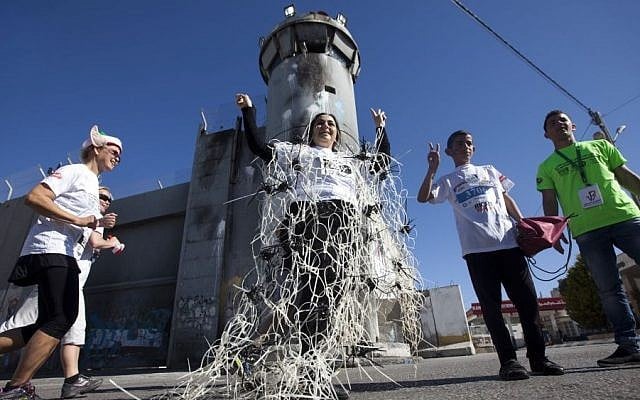A foreign activists wearing plastic handcuffs to symbolize her support for the release of Palestinian prisoners in Israeli jails, poses for a photo near the West Bank security barrier that Israel has built, during the second annual Palestine International Marathon in the West Bank town of Bethlehem, Friday, April 11, 2014 photo credit: AP/Majdi Mohammed