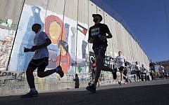 Palestinians and foreigners, including activists, run past the security barrier during the second annual Palestine International Marathon in the West Bank town of Bethlehem, Friday, April 11, 2014 (photo credit: AP/Majdi Mohammed)