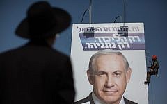 An ultra-Orthodox man looks at workers hanging a giant campaign poster showing Benjamin Netanyahu, at the entrance to Jerusalem, on March 11, 2015. (Photo credit: Yonatan Sindel/FLASH90)