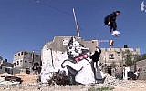 Gaza city parkour enthusiasts perform in front of graffiti by British artist Banksy in Gaza City. (screen capture: Youtube/The Guardian)