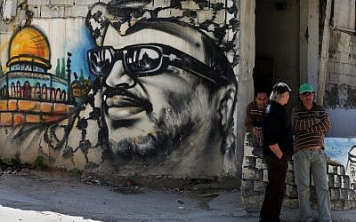 Palestinian refugees stand next to graffiti bearing a portrait of late Palestinian President Yasser Arafat at the Ain Al-Helweh refugee camp, near the southern Lebanese city of Sidon, on March 16, 2015. (photo credit: AFP / JOSEPH EID)