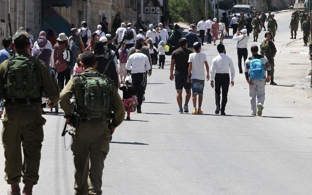 Israeli security forces guard settlers as they enter the Palestinian side of the West Bank city of Hebron to visit the tomb of Othniel Ben Kenaz, on April 5, 2015. (Photo credit: Hazem Bader/AFP)