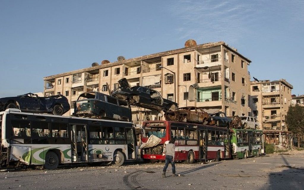 A Syrian man walks past a makeshift barricade made of wrecked buses to obstruct the view of regime snipers and to keep people safe, on April 5, 2015, in the Hanano neighborhood, in the eastern district of the northern city of Aleppo. (photo credit: Karam al-Masri/AFP)
