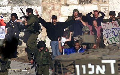 Under the cover of an Israeli army tank (foreground), Israeli soldiers arrest international peace activists holding placards outside the Church of Nativity in the West Bank town of Bethlehem, April 28, 2002. (photo credit: AP/Lefteris Pitarakis)