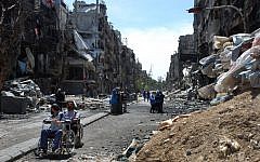 In this picture provided by the United Nations Relief and Works Agency for Palestine Refugees in the Near East, two men on their wheelchairs wait to receive food supplies at a damaged street in the besieged Yarmouk refugee camp, on the southern edge of the Syrian capital Damascus, Syria, Thursday, April 24, 2014. (AP)