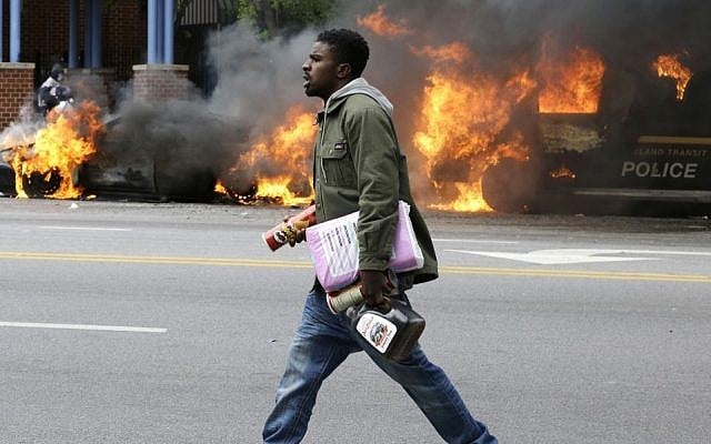 A man carries items from a store as police vehicles burn, Monday, April 27, 2015, after the funeral of Freddie Gray in Baltimore. Gray died from spinal injuries about a week after he was arrested and transported in a Baltimore Police Department van. (photo credit: AP/Patrick Semansky) 