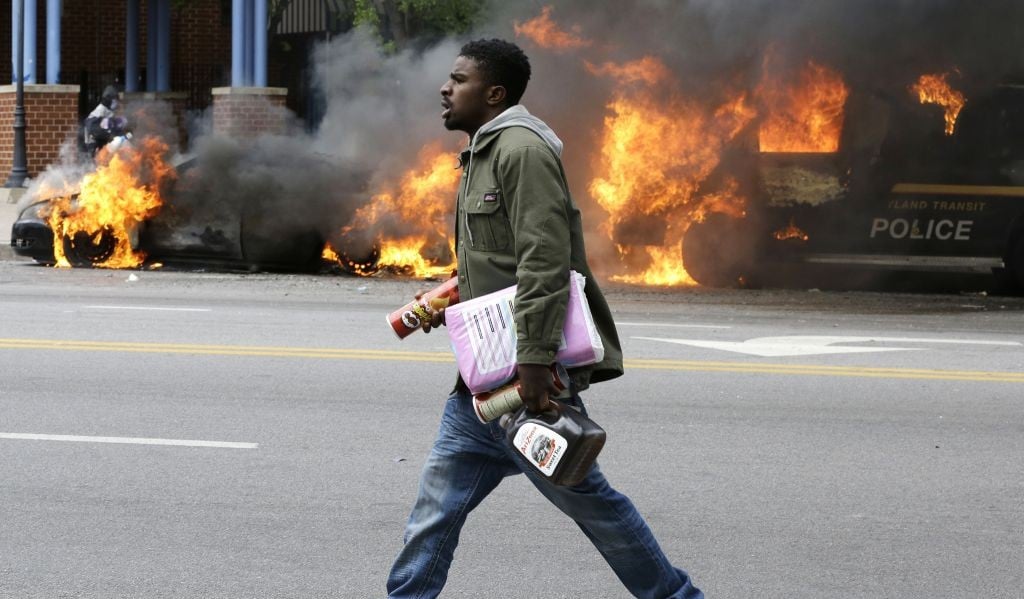 A man carries items from a store as police vehicles burn, Monday, April 27, 2015, after the funeral of Freddie Gray in Baltimore. Gray died from spinal injuries about a week after he was arrested and transported in a Baltimore Police Department van. (photo credit: AP/Patrick Semansky) A man carries items from a store as police vehicles burn, Monday, April 27, 2015, after the funeral of Freddie Gray in Baltimore. Gray died from spinal injuries about a week after he was arrested and transported in a Baltimore Police Department van. (photo credit: AP/Patrick Semansky)
