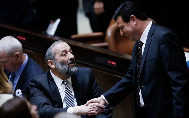 Shas party leader Aryeh Deri shakes hands with Joint Arab list head Ayman Odeh during the swearing-in ceremony for the 20th Knesset, March 31, 2015. (Photo credit: Miriam Alster/Flash90)