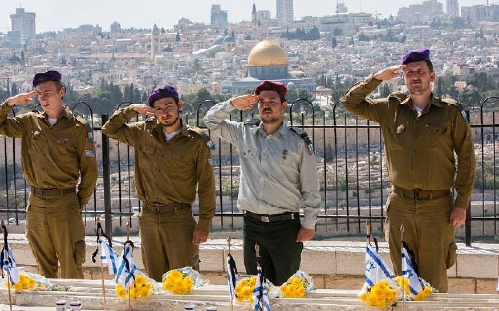 Israeli soldiers place the Israeli flag on the grave of fallen servicemen during a ceremony held at the Mount of Olives in preparation for Memorial Day, with Jerusalem's Dome of the Rock in the background, April 21, 2015 (Photo credit Yonatan Sindel/Flash90)