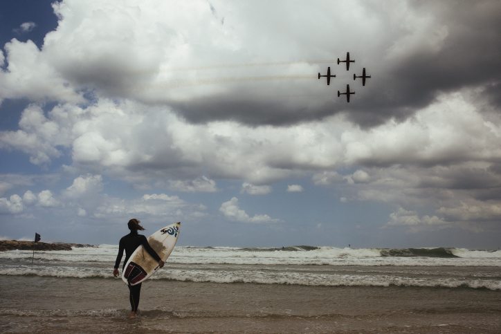 A surfer watches and Israeli Air Force aerial acrobatics demonstration on the 67th Independence Day of Israel over the beach in Tel Aviv on April 23, 2015. (Photo credit: Matanya Tausig/Flash90) A surfer watches and Israeli Air Force aerial acrobatics demonstration on the 67th Independence Day of Israel over the beach in Tel Aviv on April 23, 2015. (Photo credit: Matanya Tausig/Flash90)