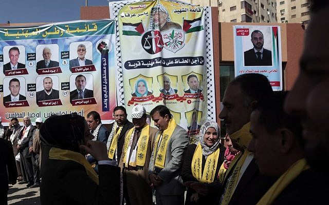 In this Monday April, 6, 2015 photo, Palestinian lawyers wear yellow Fatah scarves as they stand in front of a poster of the Fatah candidates for the lawyers' union elections outside the bar association office in Gaza City (photo credit: AP/Khalil Hamra)