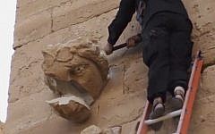 A piece falls off from a curved face on the wall of an ancient building as a militant hammers it in Hatra, Iraq, a large fortified city recognized as a UNESCO World Heritage site, April 3, 2015 (Photo credit: AP Photo/Militant video)