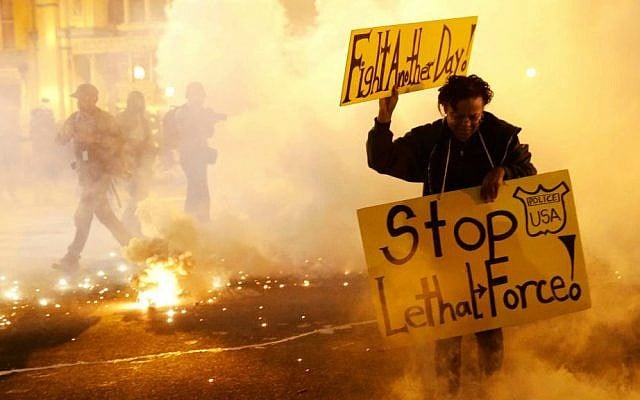 A woman runs for safety as police throw tear gas canisters while enforcing curfew, Tuesday, April 28, 2015, in Baltimore, a day after unrest that occurred following Freddie Gray's funeral. (AP Photo/Patrick Semansky)