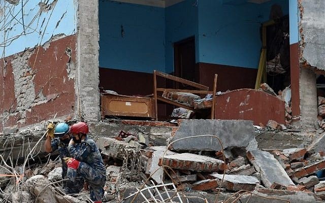 Two Nepalese search and rescue team members watch a US team work at the site of a collapsed building in Kathmandu on April 30, 2015. (Photo credit: AFP/ROBERTO SCHMIDT)