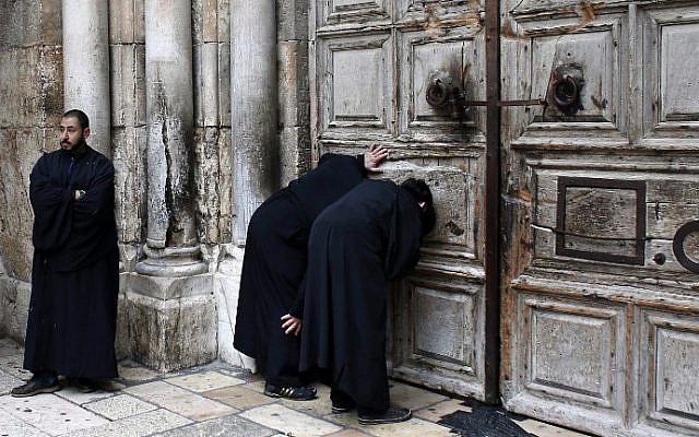 Christian Orthodox priests look through a hole in the main door of the Church of the Holy Sepulcher, before the Holy Fire ceremony around Jesus's tomb, in Jerusalem’s Old City, on April 11, 2015. (AFP/Thomas Coex) Christian Orthodox priests look through a hole in the main door of the Church of the Holy Sepulcher, before the Holy Fire ceremony around Jesus's tomb, in Jerusalem’s Old City, on April 11, 2015. (AFP/Thomas Coex)