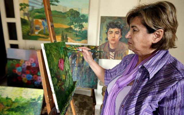 Mariam Saidi paints as she stands in front of an oil painting of her son Maher (center-background), who disappeared in 1982 at the age of 15 while fighting near Beirut, at her house in the Lebanese capital on April 8, 2015. (photo credit: AFP/Joseph Eid)