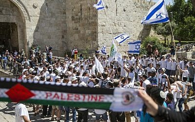 Palestinian women hold a scarf bearing the Palestine name as Israeli youths carry their national flag in the "flag march" through Damascus Gate in Jerusalem's Old City during celebrations for Jerusalem Day on May 17, 2015. (AFP Photo/Jack Guez)