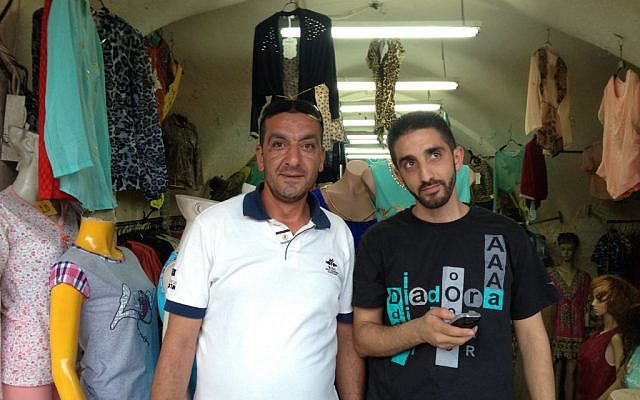 Ahmad al-Dabbagh, left, stands in front of a clothing shop in the Muslim Quarter that decided to remain open in defiance of police instructions (Elhanan Miller/Times of Israel)