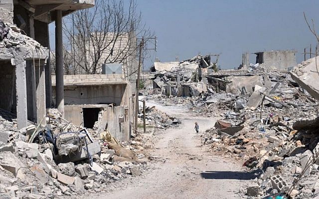 In this picture taken on Saturday, April 18, 2015, a Kurdish boy, center background, walks between buildings that were destroyed during the battle between the US backed Kurdish forces and the Islamic State fighters, in Kobani, north Syria. (Photo credit: AP/Mehmet Shakir)