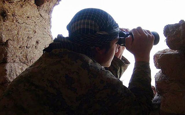 In this photo released on March 23, 2015, by a jihadist website, which has been verified and is consistent with other AP reporting, an Islamic State fighter uses his binoculars as he looks at Kurdish fighters at a front line near Tel Abyad, northeast Syria. (Jihadist website via AP)