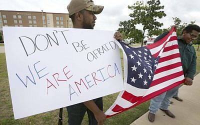 Joseph Offutt, left, and Raheem Peters hold a sign and a U.S. flag across the street from the Curtis Culwell Center, Tuesday, May 5, 2015, in Garland, Texas. A man, whose social media presence was being scrutinized by federal authorities, was one of two suspects killed in the Sunday shooting at this location that hosted a cartoon contest featuring images of the Muslim Prophet Muhammad. The Islamic State group on Tuesday claimed responsibility for the attack. (photo credit: AP/LM Otero)
