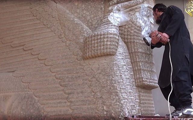In this image made from video posted on a social media account affiliated with the Islamic State group on Thursday, Feb. 26, 2015, a militant uses a power tool to destroy a winged-bull Assyrian protective deity at the Ninevah Museum in Mosul, Iraq. (Photo credit: AP via militant social media account, File)