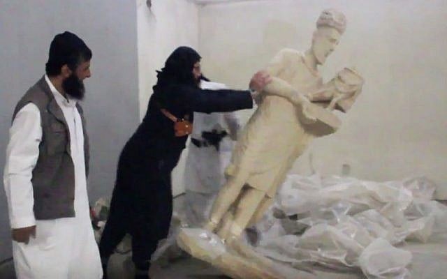 In this image made from video posted on a social media account affiliated with the Islamic State group on Thursday, Feb. 26, 2015, a militant topples an ancient artifact in the Ninevah Museum in Mosul, Iraq. (Photo credit: AP via militant social media account, File)