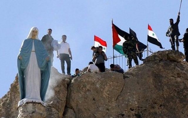 Members of the Syrian National Defense Forces (NDF) stand behind a statue of Virgin Mary perched on the cliffs overlooking the ancient Christian town of Maalula, 56 kilometers northeast of the Syrian capital Damascus, on June 13, 2015 after the statue was restored to its original place. (AFP PHOTO / LOUAI BESHARA)