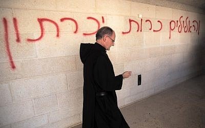 A priest walks past graffiti reading in Hebrew, 'false idols will be eliminated,' as he inspects the damage at the Church of the Multiplication at Tabgha, on the shores of the Sea of Galilee in northern Israel, June 18, 2015 (AFP/Menahem Kahana) A priest walks past graffiti reading in Hebrew, 'false idols will be eliminated,' as he inspects the damage at the Church of the Multiplication at Tabgha, on the shores of the Sea of Galilee in northern Israel, June 18, 2015 (AFP/Menahem Kahana)