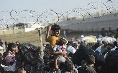 A man carries a girl as Syrians fleeing the war pass through broken down border fences to enter Turkish territory illegally, near the Turkish Akcakale border crossing, the southeastern Sanliurfa province, on June 14, 2015. (AFP PHOTO/BULENT KILIC)