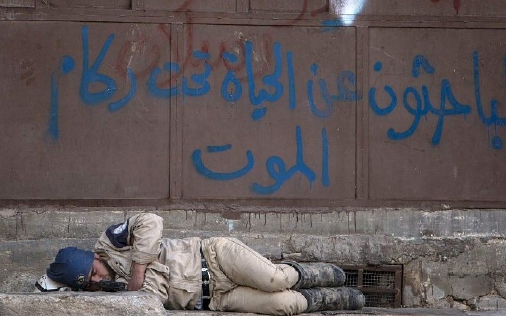 A member of the civil defense sleeps on the street in the rebel-held side of Syria's northern city of Aleppo on June 8, 2015. Arabic graffiti in blue reads: "Those looking for life under the rubble of death". (Karam al-Masri/AFP)