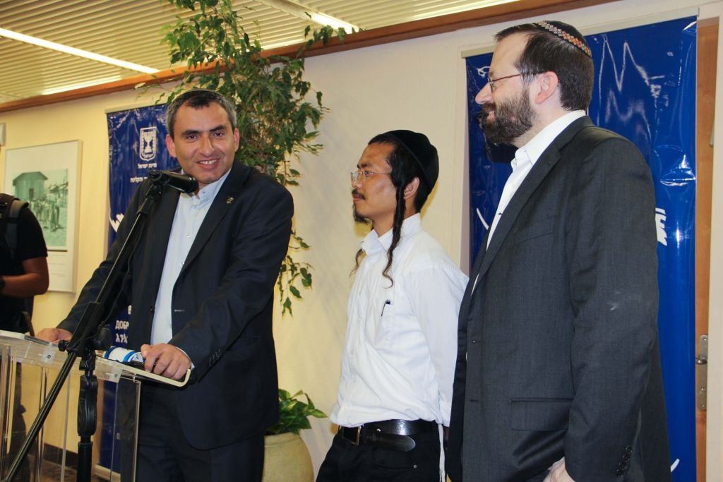 IMG_5135-2 Absorption Minister Ze'ev Elkin (L) speaks to a gathering of new immigrants from India, alongside his translator (C) and Shavei Israel director Rabbi Michael Freund (R) on June 18, 2015. (Laura Ben-David/Shavei Israel)
