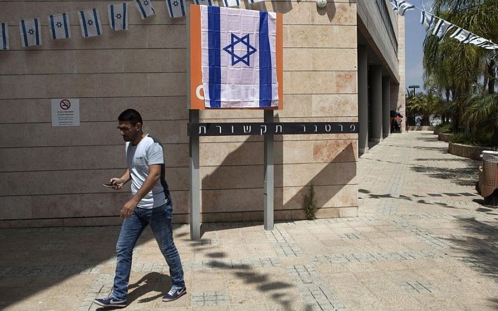 An Israeli man walks past the Orange company logo covered with an Israeli flag at the Partner Orange offices in the city of Rosh Ha'ayin, Israel. Thursday, June 4, 2015. (AP Photo/Dan Balilty)