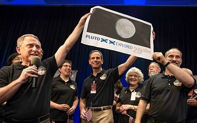 In this photo provided by NASA, New Horizons Principal Investigator Alan Stern of Southwest Research Institute (SwRI), Boulder, Colo., left, Johns Hopkins University Applied Physics Laboratory (APL) Director Ralph Semmel, center, and New Horizons Co-Investigator Will Grundy of the Lowell Observatory hold a print of a US stamp with their suggested update since the New Horizons spacecraft made its closest approach to Pluto, at the Johns Hopkins University Applied Physics Laboratory (APL) in Laurel, Md. on Tuesday, July 14, 2015. (Bill Ingalls/NASA via AP)