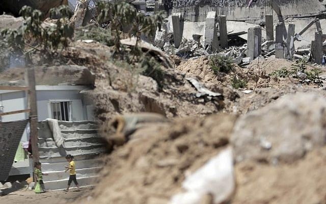 In this June 17, 2015 photo, Palestinian girls are seen reflected in a mirror as they walk next to rubble in the area where they live with family after losing their house in Gaza City. (AP/Khalil Hamra)