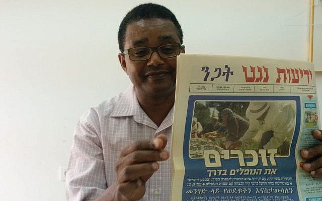 Dr. Anbessa Teferra, a professor of Semitic languages at Tel Aviv University, with a copy of Yedioth Negat, an Amharic newspaper. (Ilan Ben Zion/Times of Israel staff)